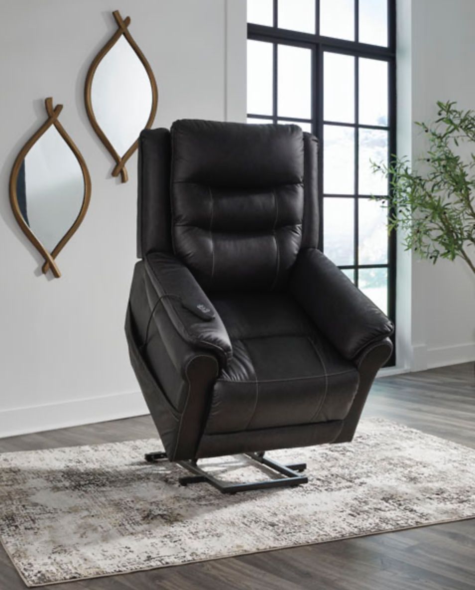 Black lift recliner chair on a rug, next to a window and decorative mirrors.