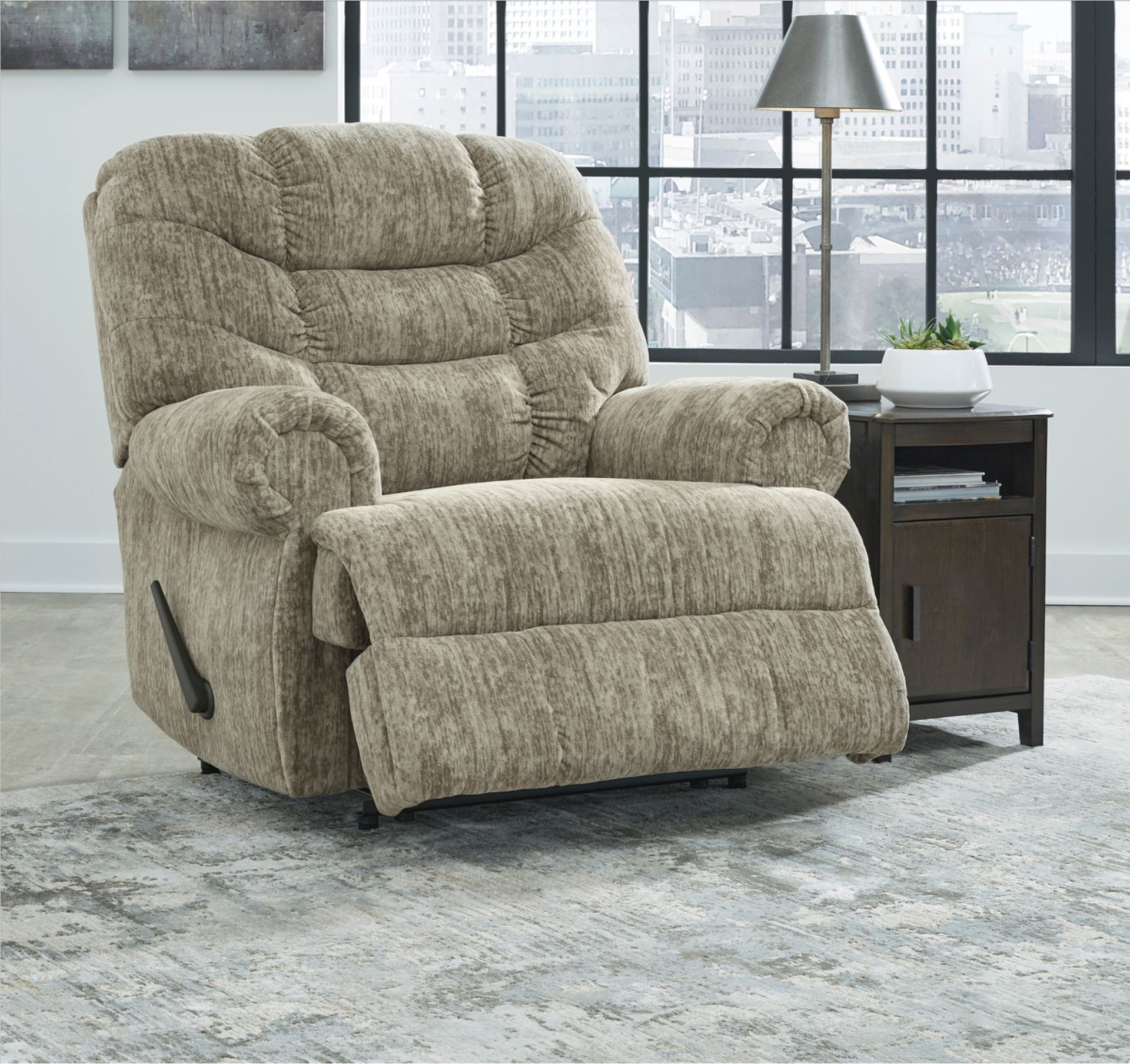 Beige reclining armchair next to a dark side table with a lamp, set on a patterned rug near a window.