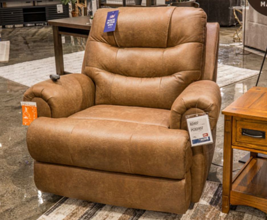Brown leather recliner chair with remote control, on display in a showroom setting.