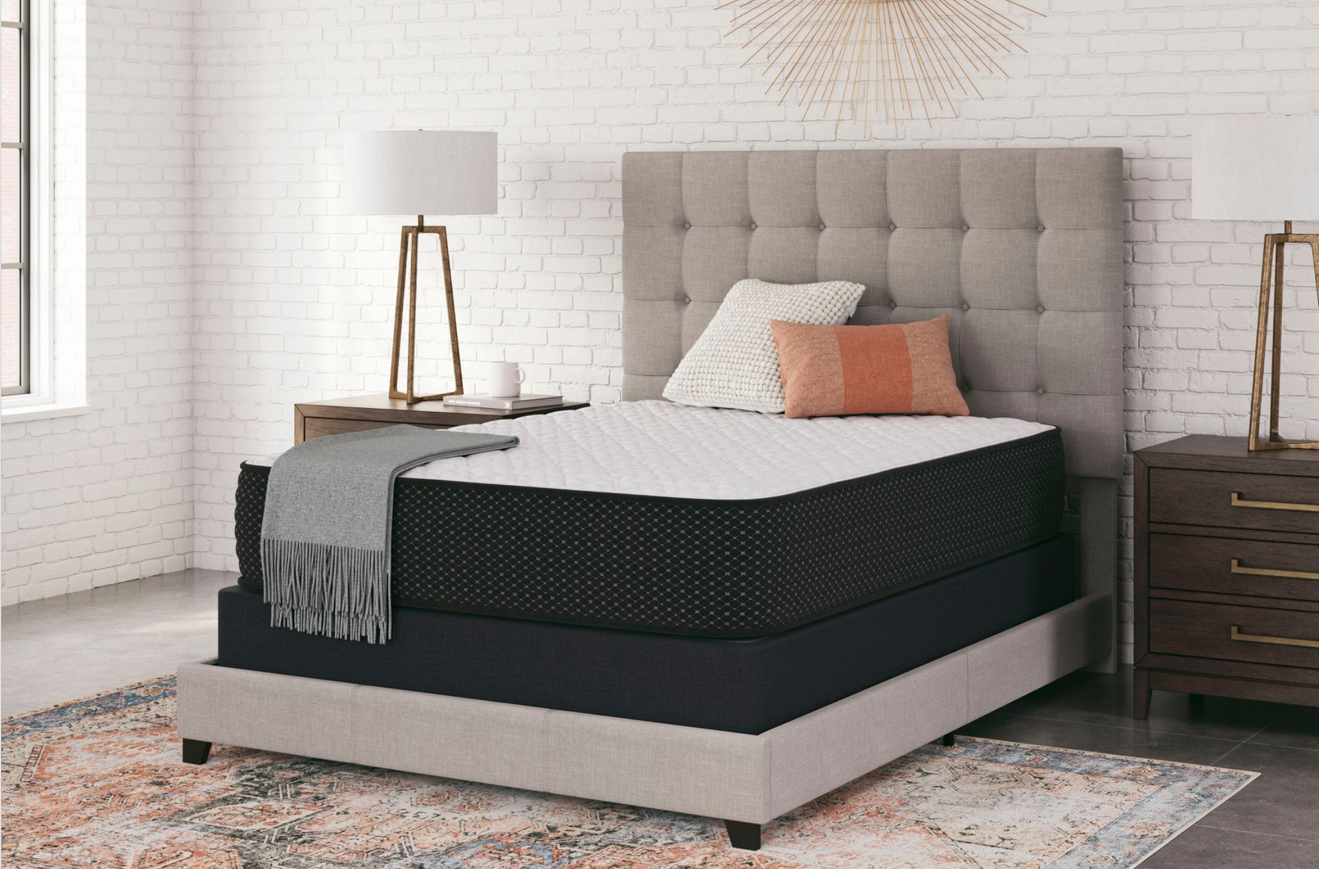 Bedroom scene: bed with gray headboard, mattress, nightstands, lamp, rug.