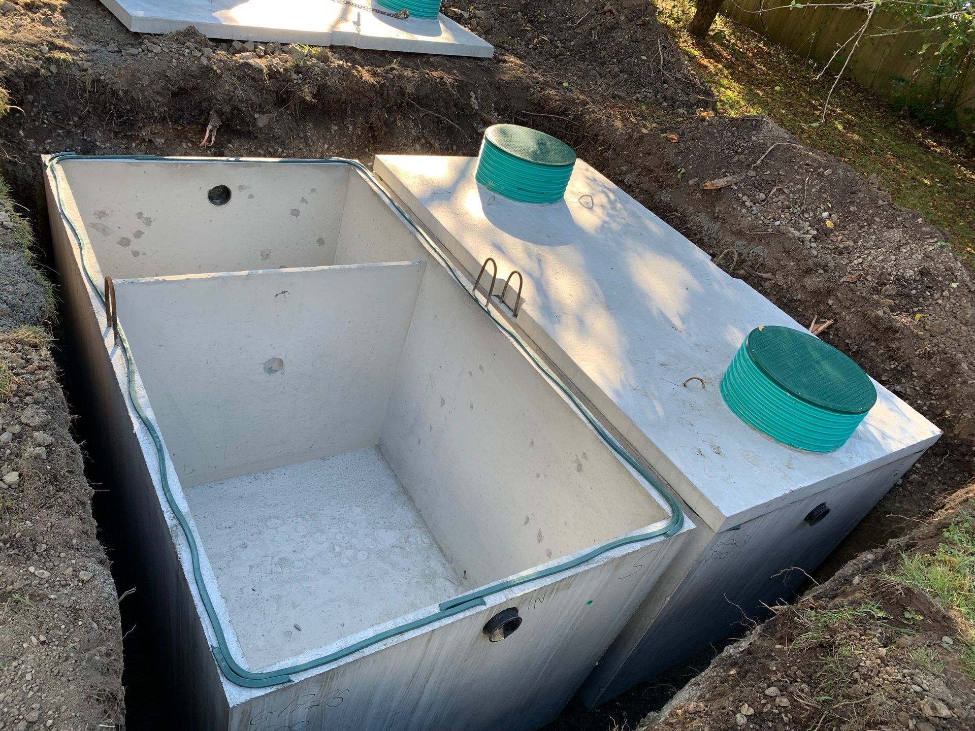 A black drainage system installed in a trench, surrounded by dirt and grass, with a worker in the background.