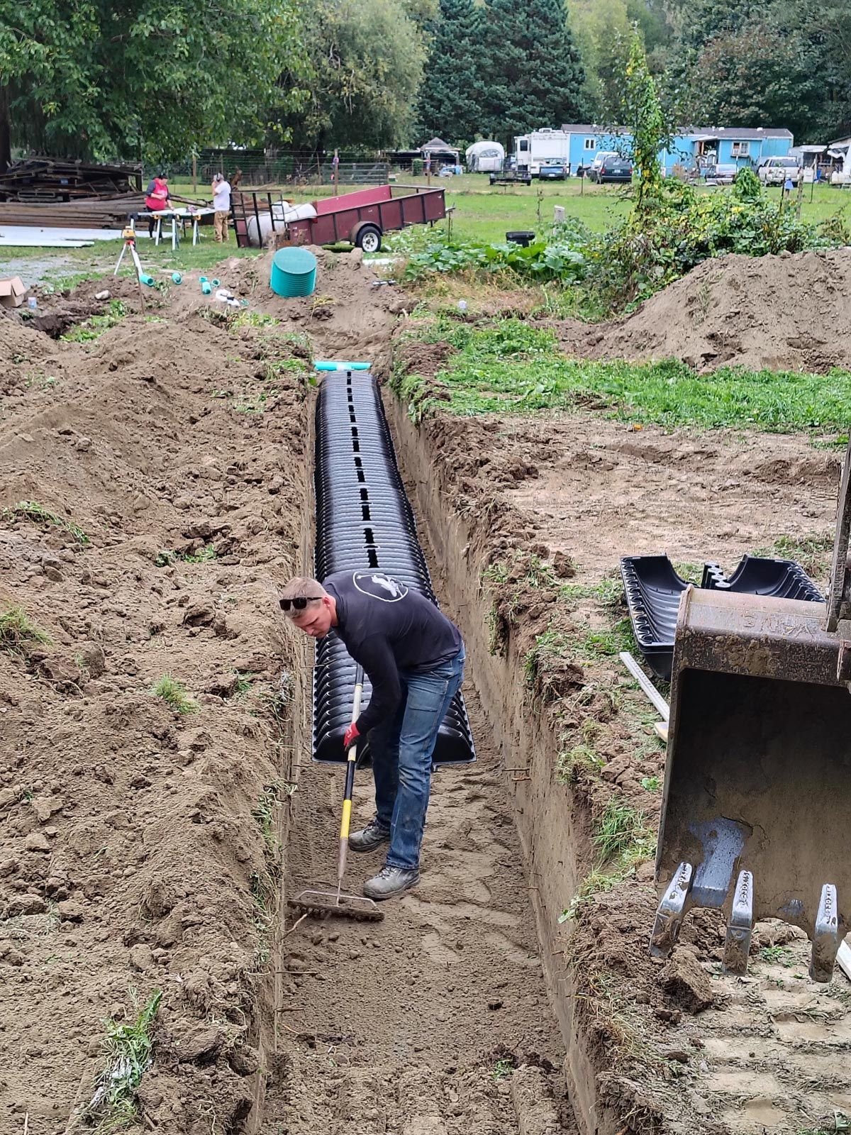 Man raking soil in trench next to plastic structure outdoors, possibly for a septic system.