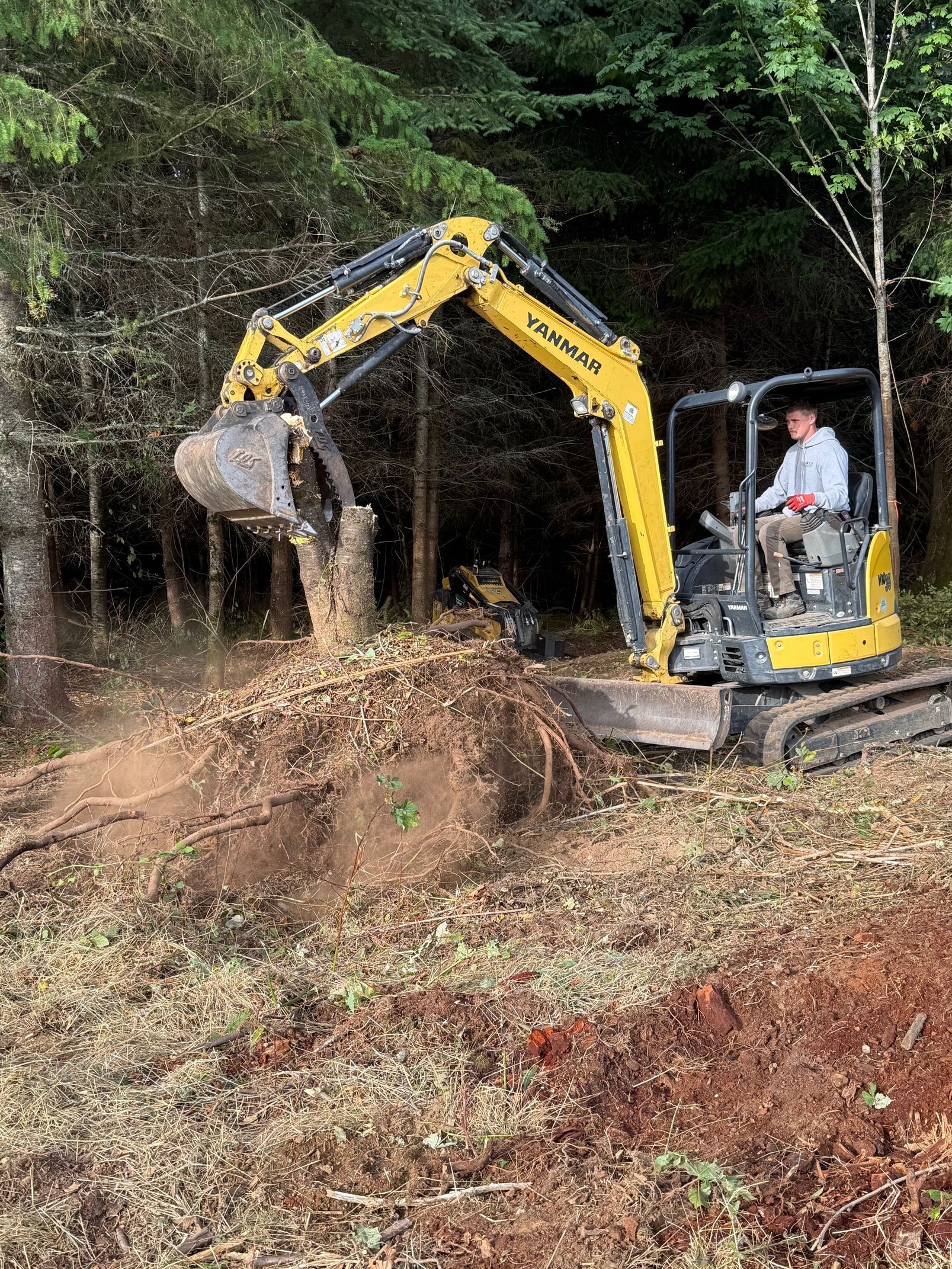 A crane lifting a large concrete septic tank in a gravel yard near a shed and trees.