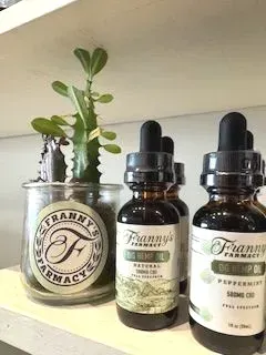 Bottles of Franny's Farmacy CBD hemp oil on a shelf, with a small plant in a glass jar.
