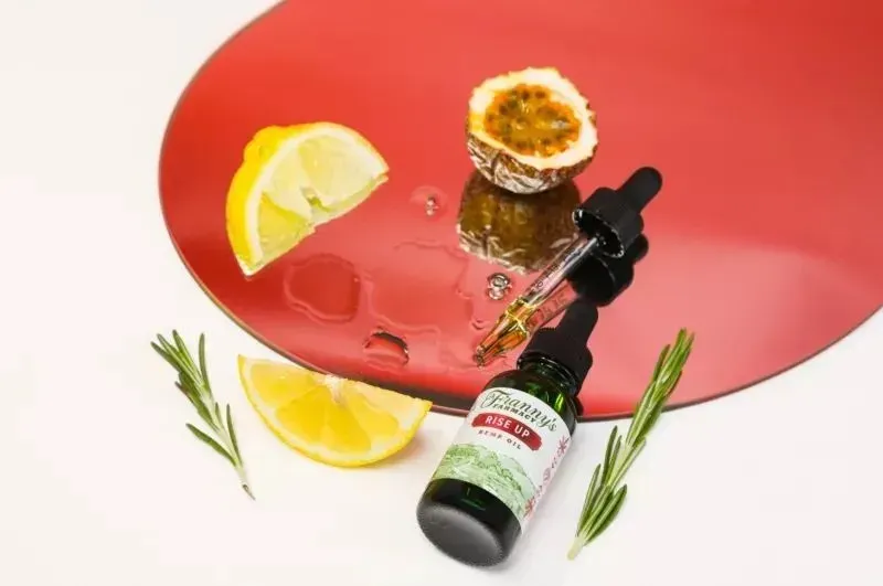 Franny's Farmacy CBD tincture bottle with dropper, lemon slices, passion fruit half, rosemary, on a red mirror