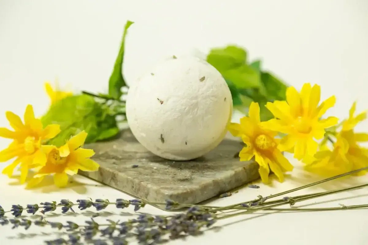 A CBD Bath bomb on a stone slab, surrounded by yellow flowers, green leaves, and lavender sprigs; white background.
