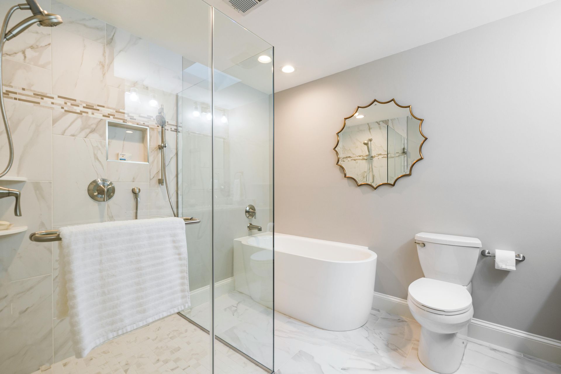 A clean modern white marbled bathroom with a standalone tub and gold trimmings