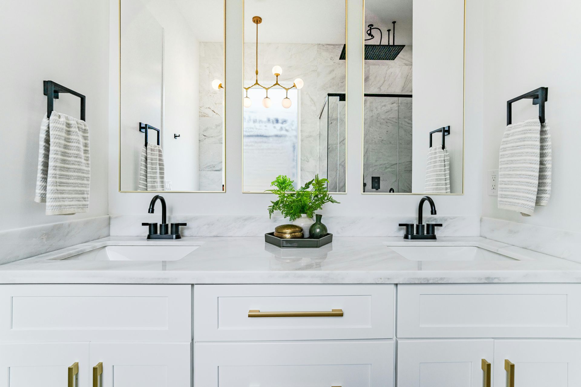 Modern and clean white double vanity with white cabinets, gold handles, and aged bronze fixtures.