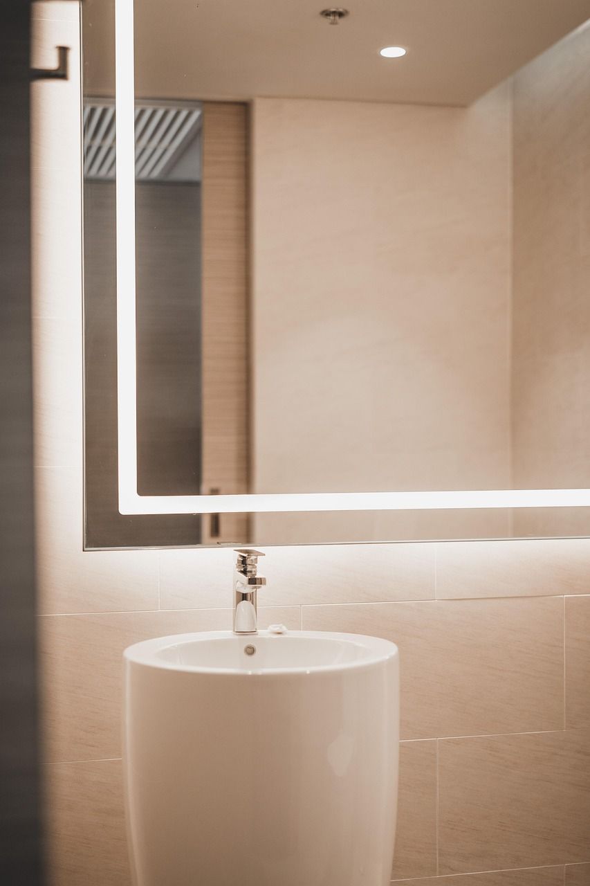 A sleek light brown open-concept bathroom with backlit mirror, standalone tub, and multiple canned lights