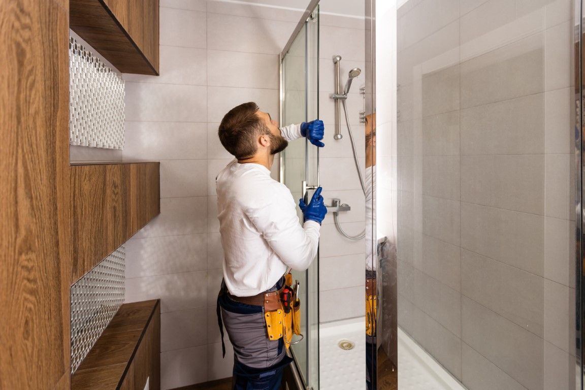 A male worker installs a clear glass shower door