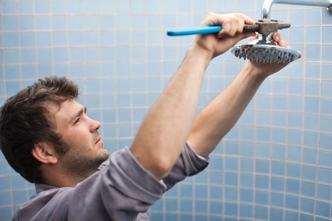 A male worker installing a showerhead in a blue tiled shower