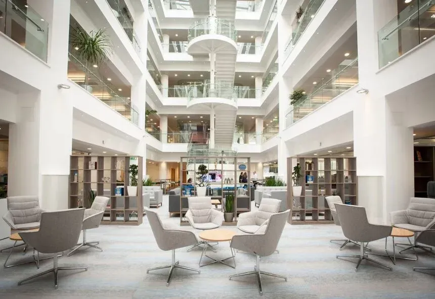 Interior view of a modern office building atrium with multiple floors, white walls, and seating areas.