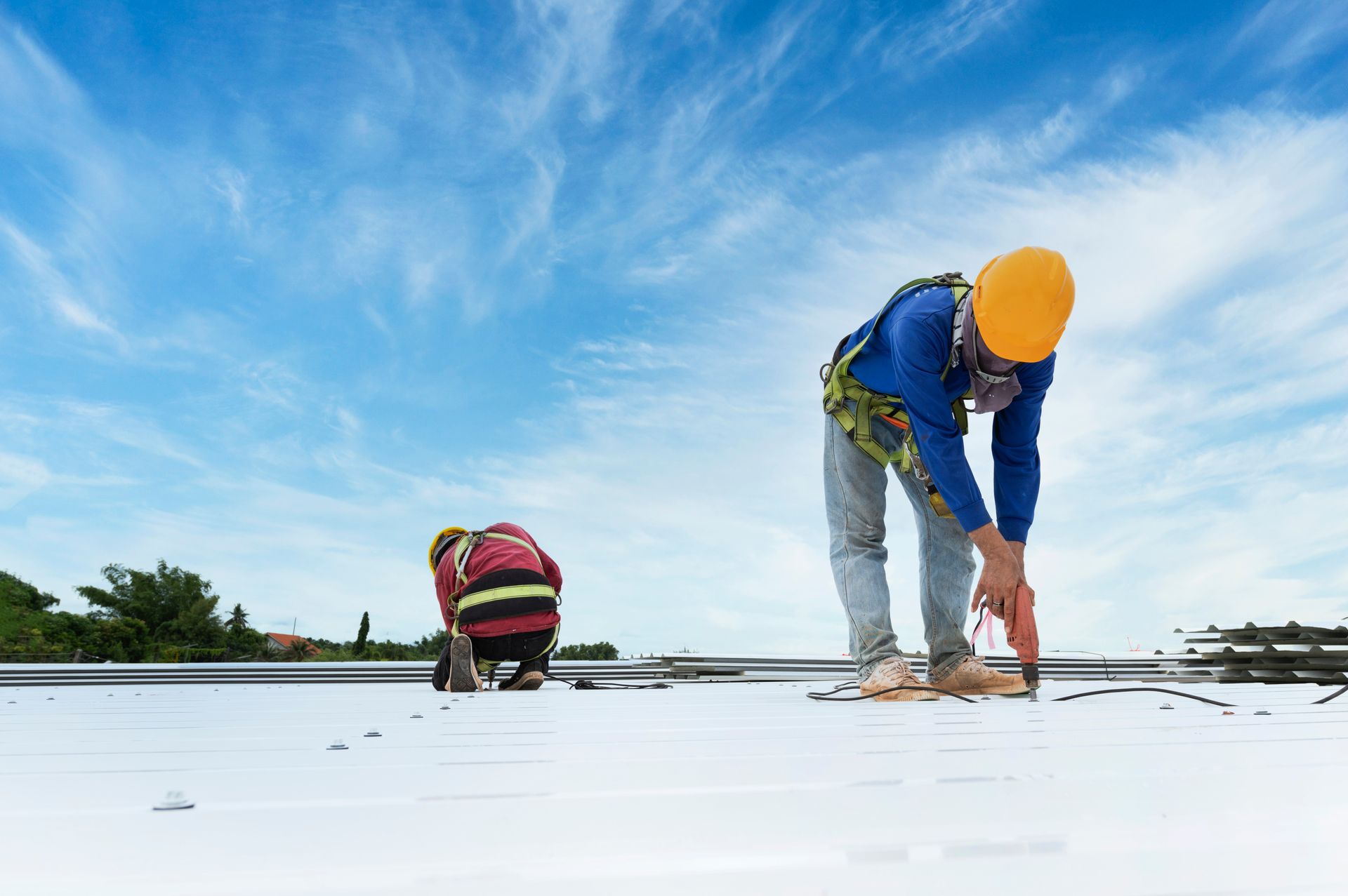 Two workers install metal roofing panels using power tools on a commercial building roof. Two workers install metal roofing panels using power tools on a commercial building roof.