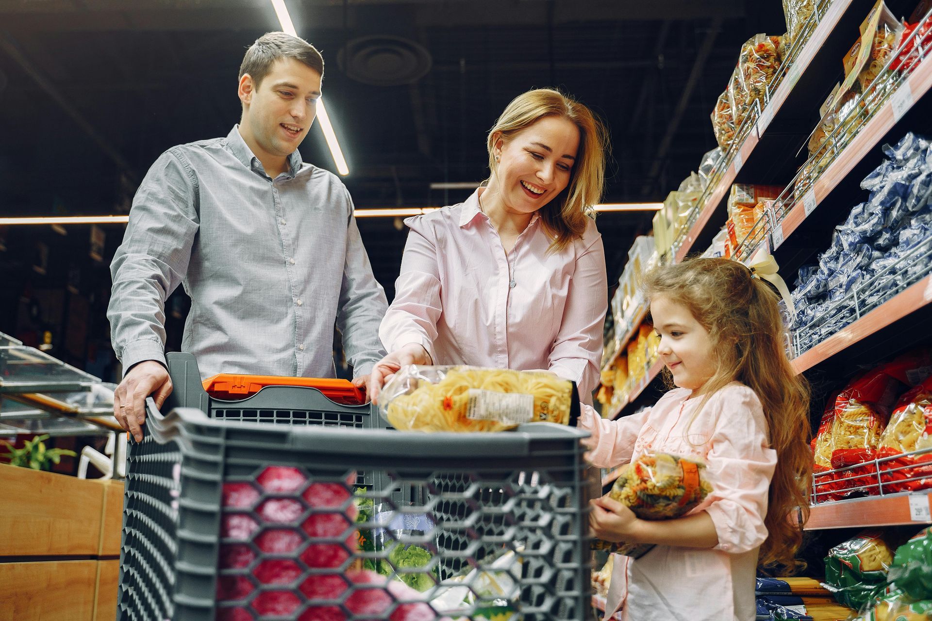 Family of three shopping in a grocery store: mother, father, and daughter, choosing food. The child is holding a product.