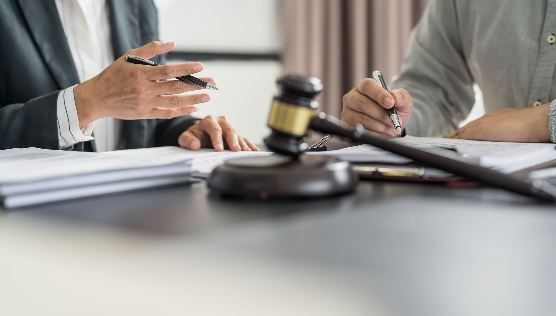 A close-up of a gavel on a table, with two people in business attire consulting documents.