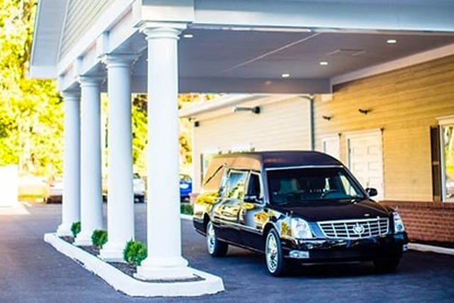 a funeral car is parked under a canopy in front of a building .