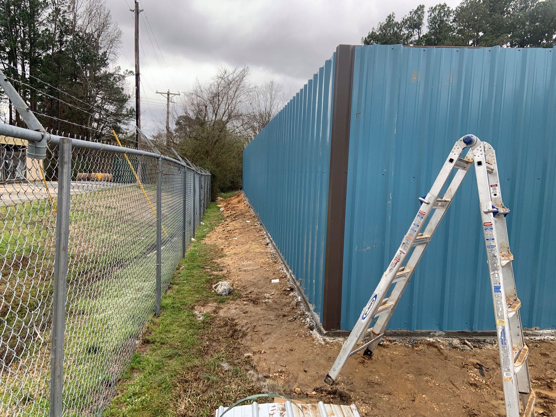 A ladder is leaning against a blue fence next to a chain link fence.