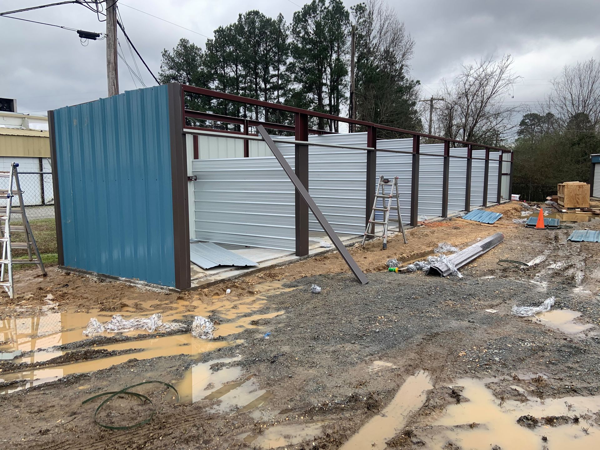 A blue metal building is being built in a muddy field.