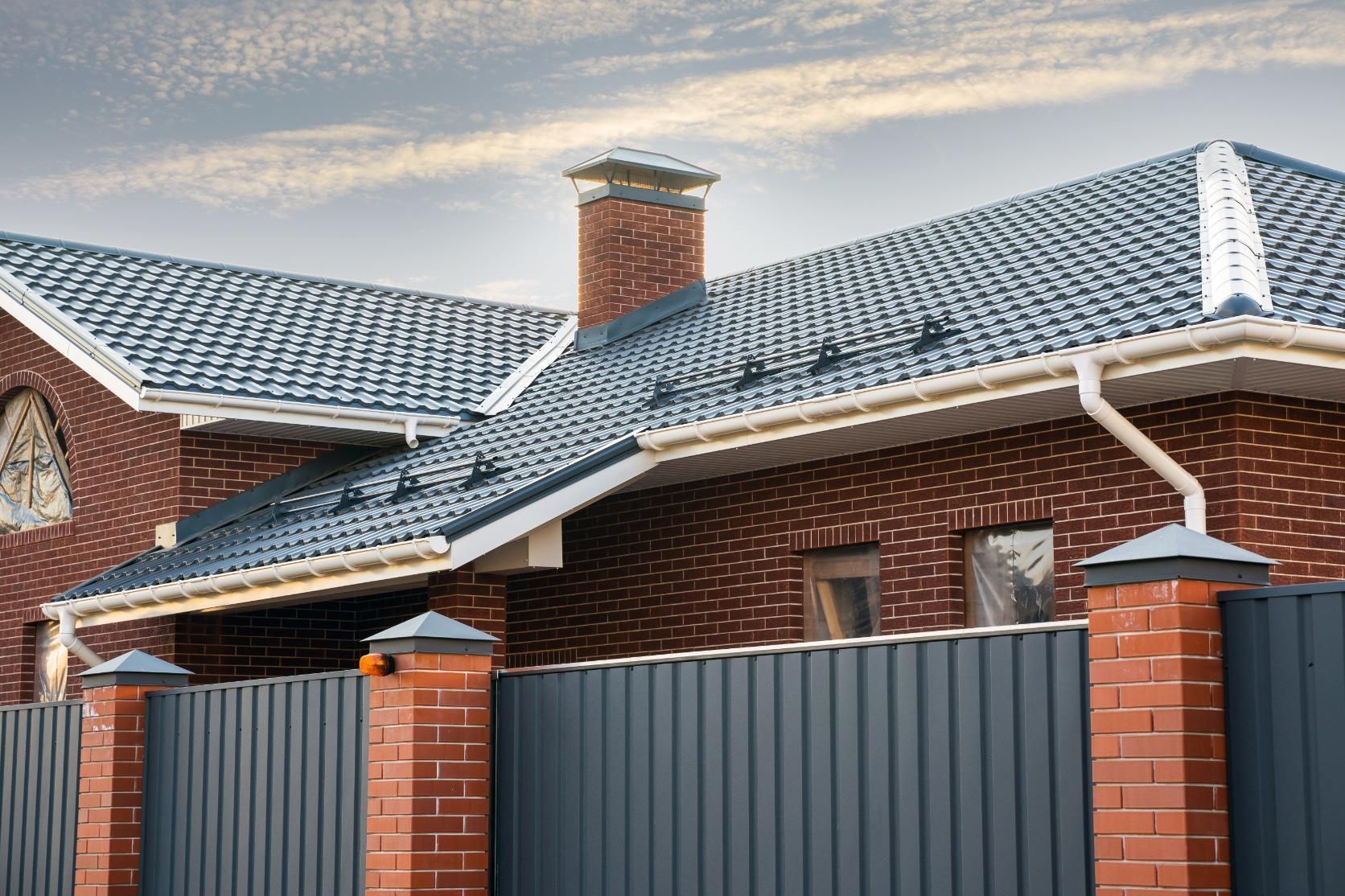 A brick house with a blue roof and a black fence.