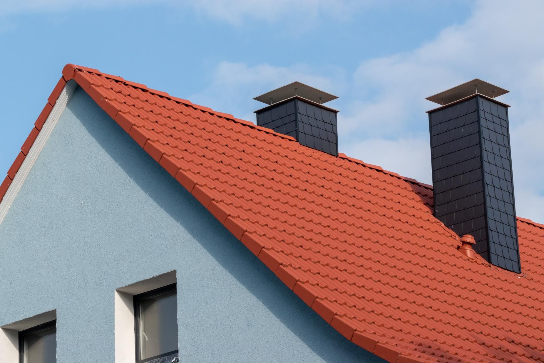 A blue house with a red roof and chimneys.