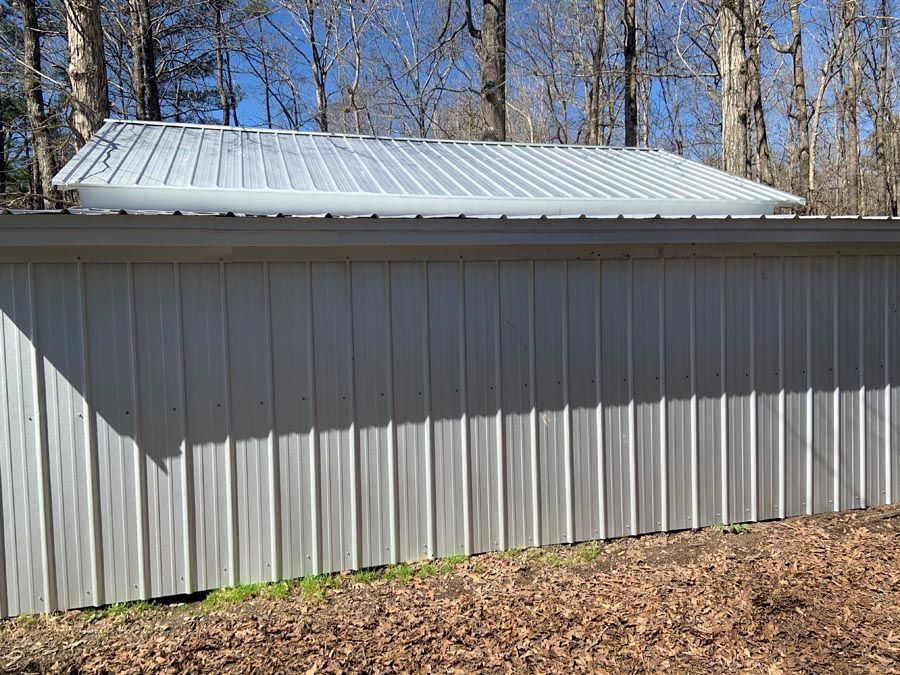 A white metal building with a roof is sitting on top of a dirt field.