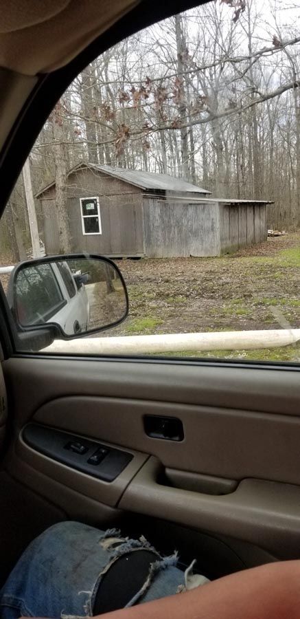 A person is sitting in a car looking out the window at a shed.