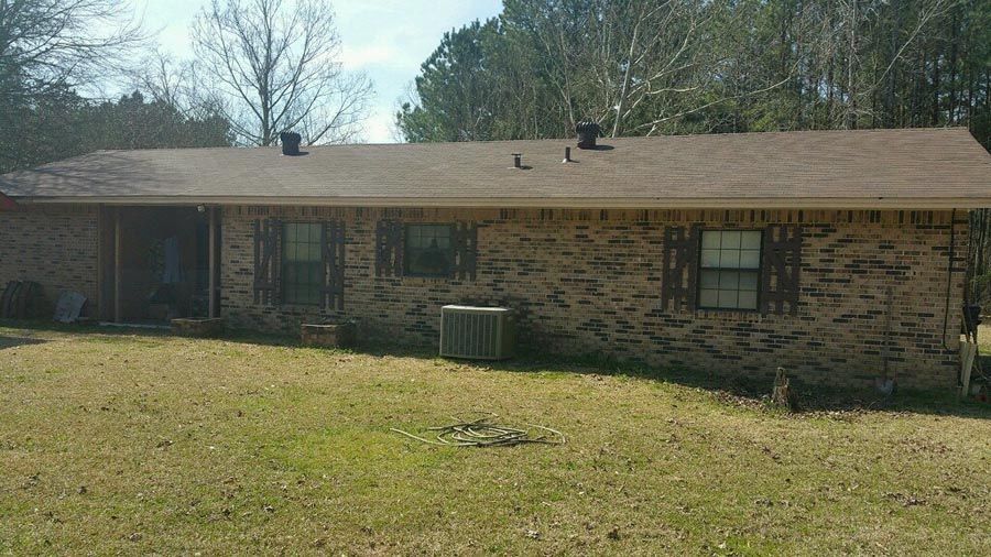 A brick house with a brown roof is sitting on top of a lush green field.