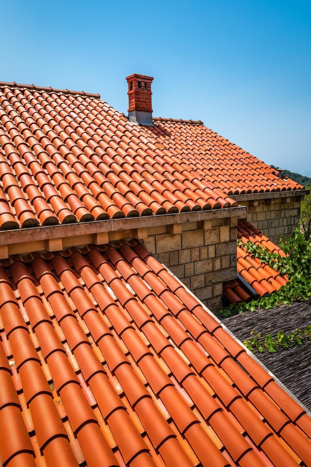 The roof of a house with red tiles and a chimney.