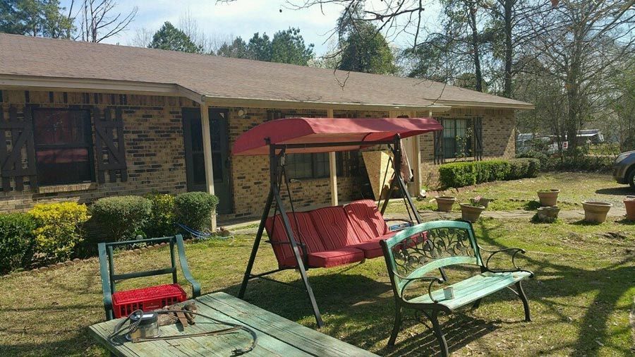 A house with a swing and benches in front of it.