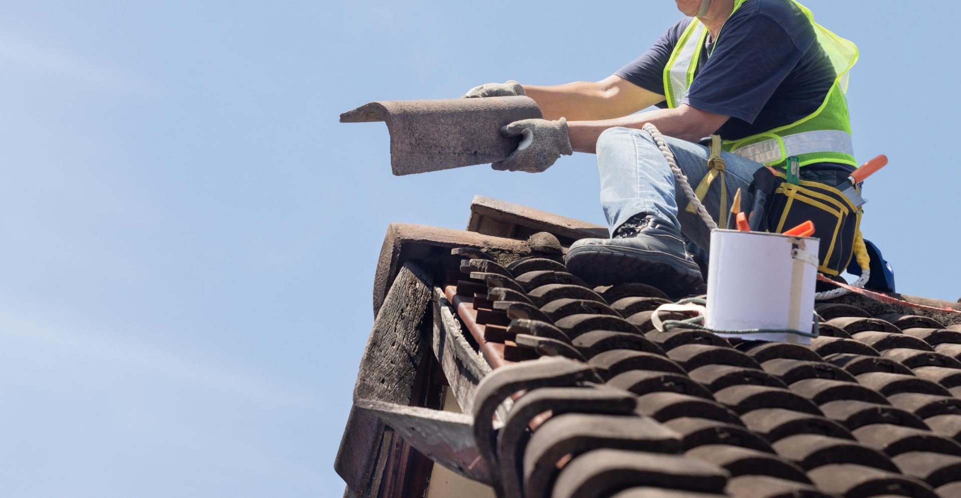 A man is sitting on top of a tiled roof working on it.