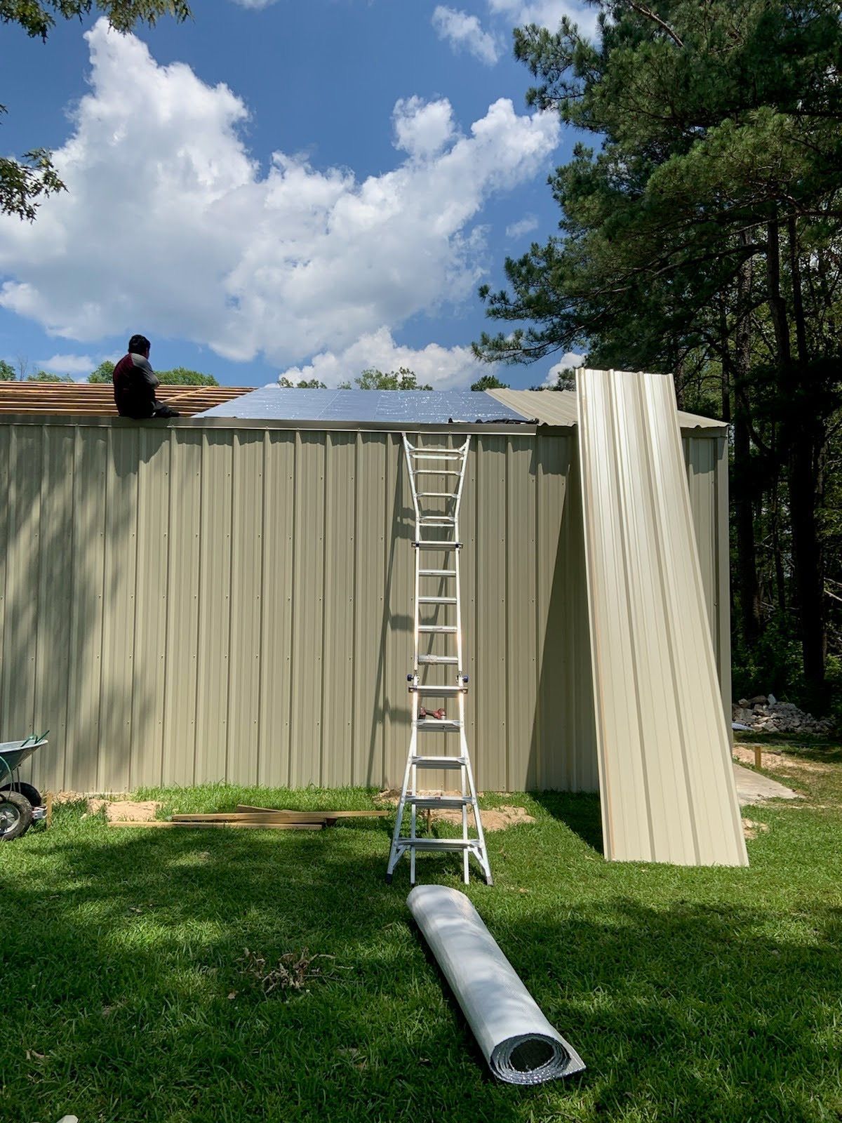 A man is sitting on top of a metal building with a ladder.