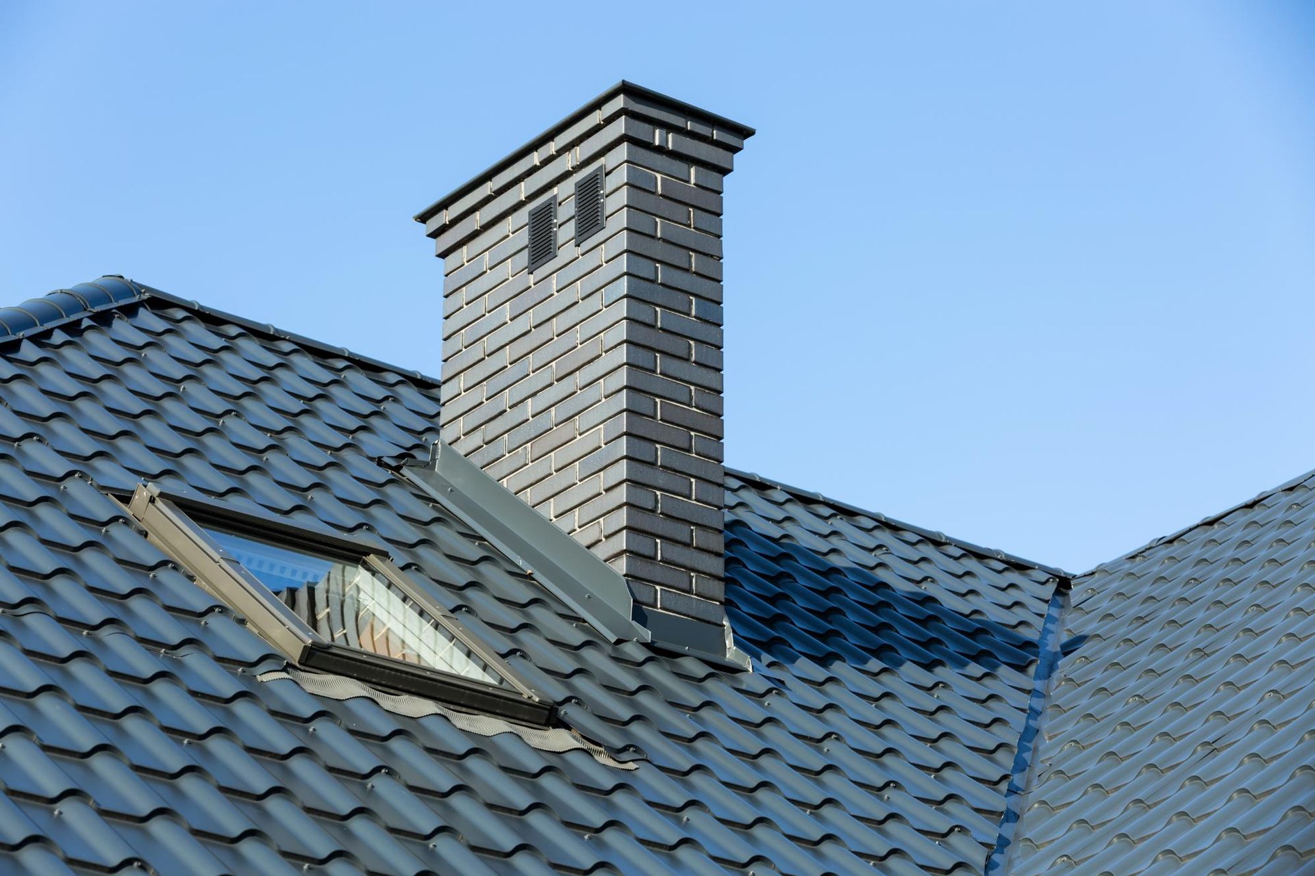 A roof with a chimney and a skylight on it.