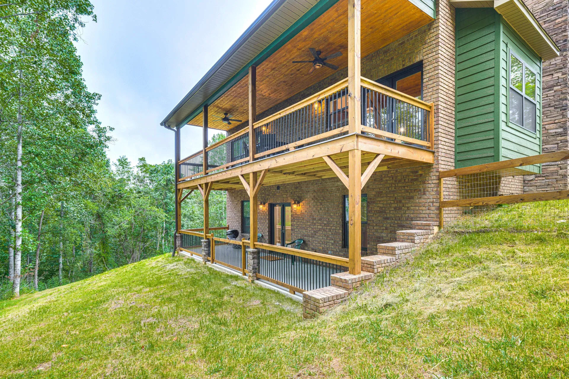 Rustic wooden cabin with covered porch on a grassy hillside, surrounded by trees