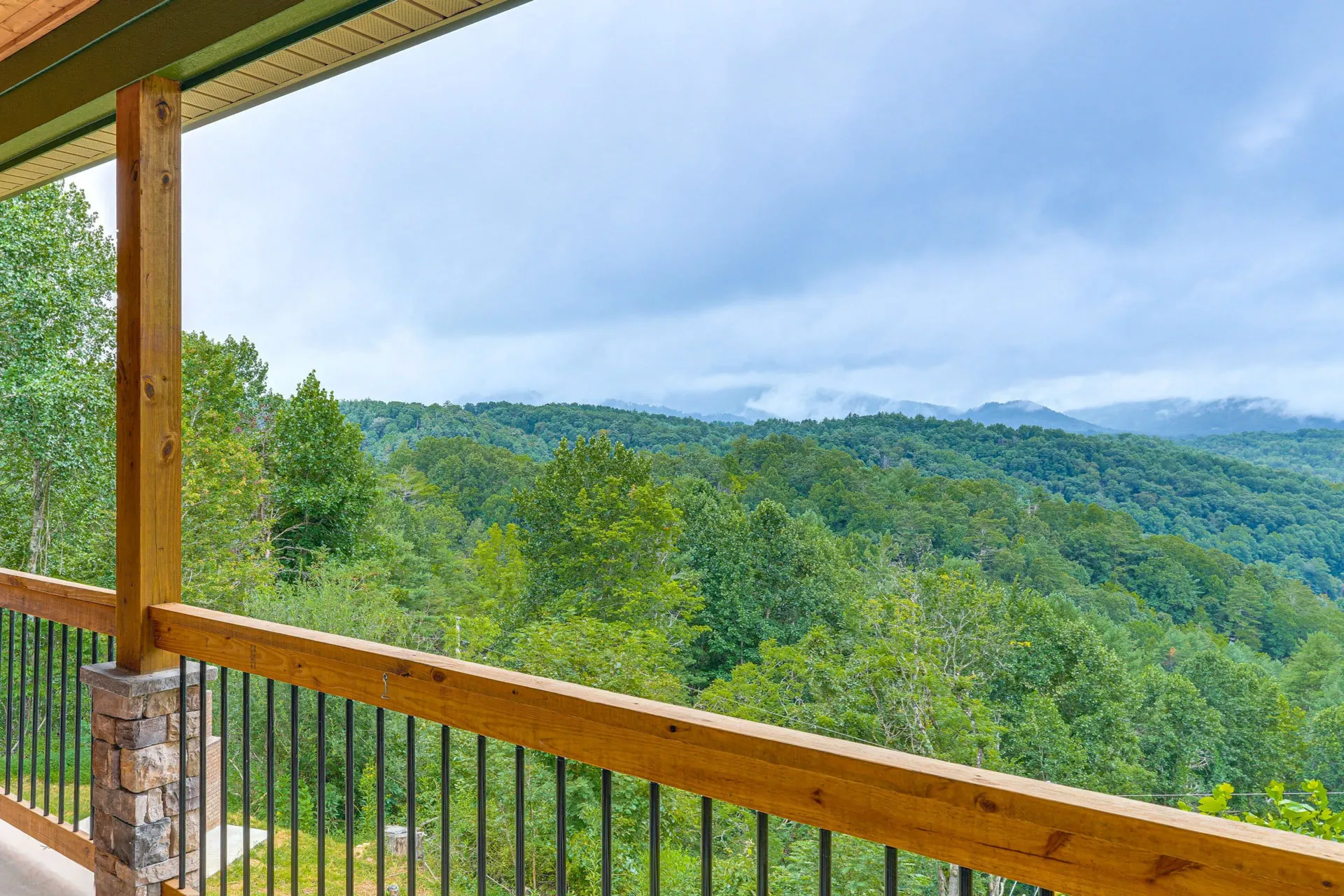 Wooden porch overlooking a lush green forested valley and distant misty hills