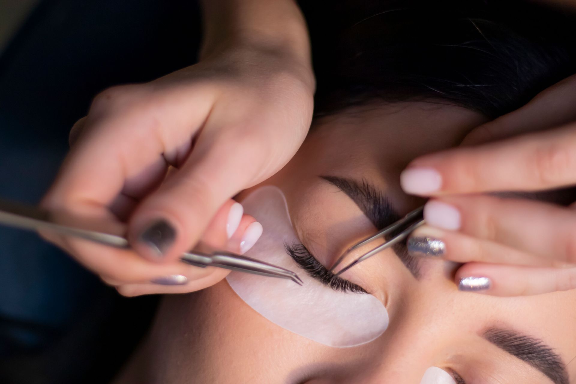 Close-up of hands performing an eyelash lift with tweezers to a closed eye