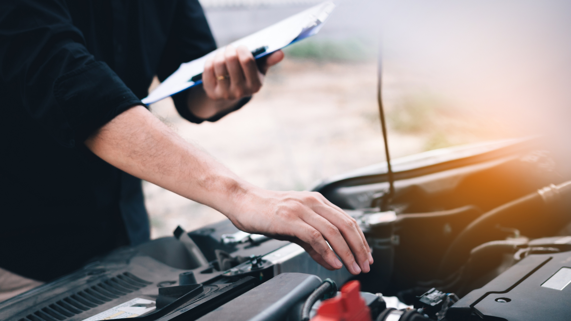 A man is looking under the hood of a car while holding a clipboard.
