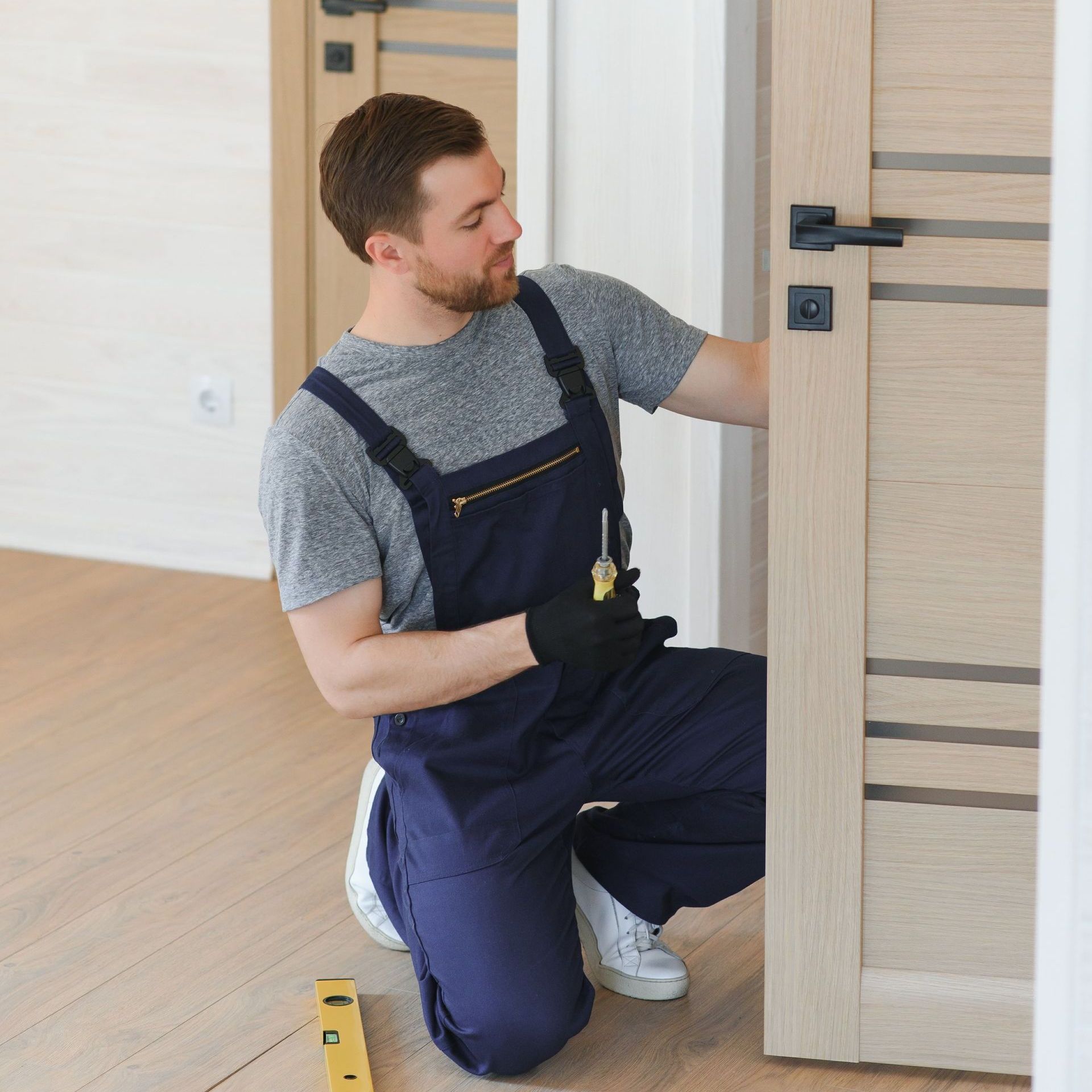 a man is kneeling down in front of a door holding a screwdriver .