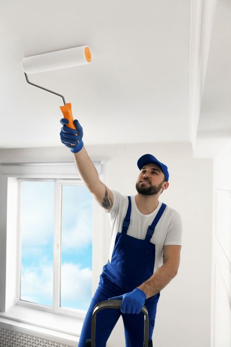 a man is painting the ceiling with a paint roller .