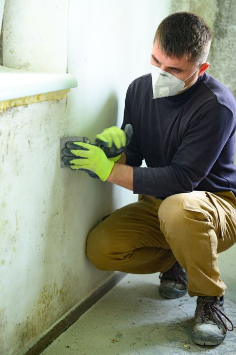 a man wearing a mask and gloves is cleaning a wall .