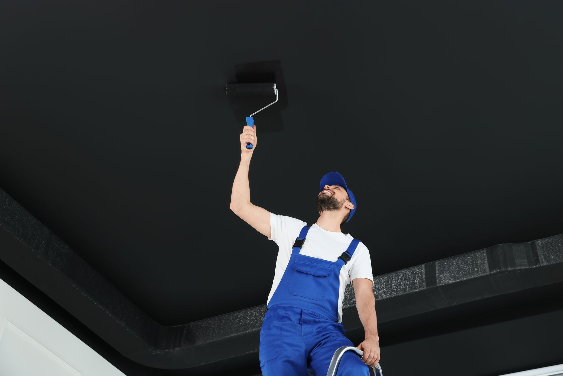 a man is painting a black ceiling with a paint roller .