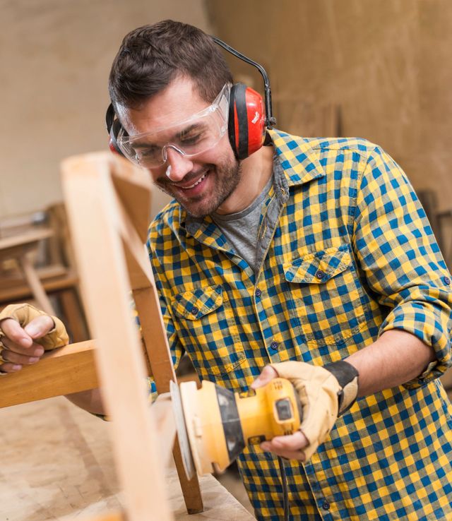 a man wearing ear muffs and goggles is sanding a piece of wood .