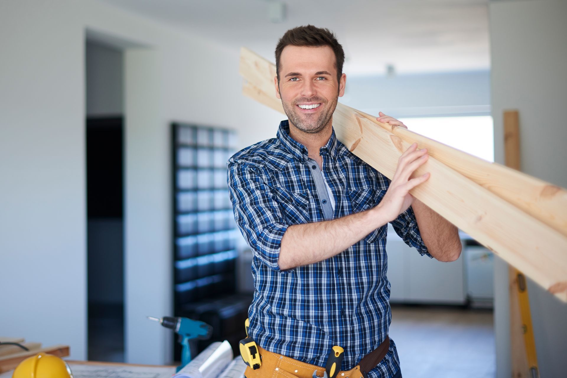 a man in a plaid shirt is holding a piece of wood .