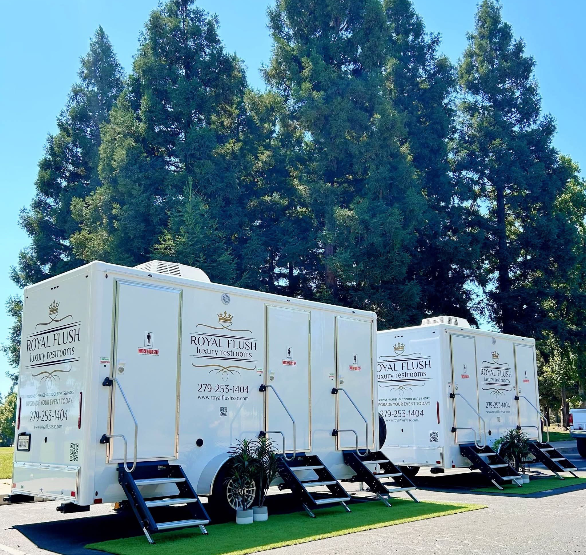 White luxury portable restrooms with steps, against a backdrop of trees and a sunny sky.