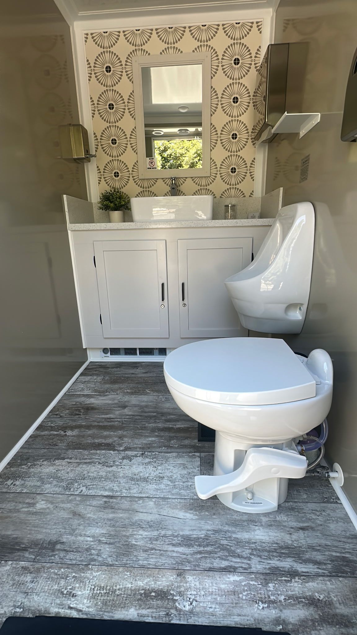 Modern bathroom with white vanity, round mirror, patterned tile wall, and white toilet on a gray rug.