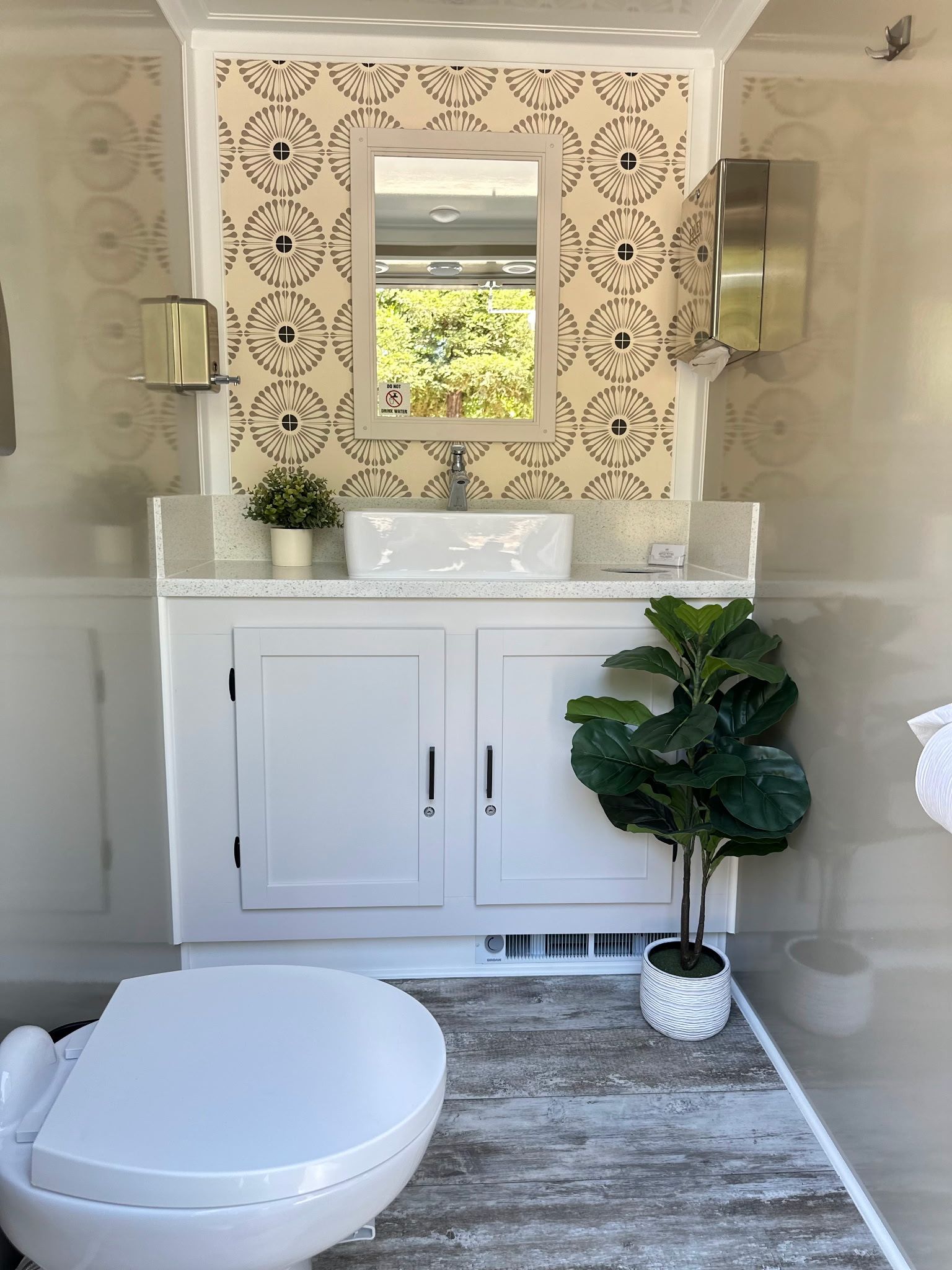 Elegant powder room with white vanity, ornate mirror, patterned wallpaper, and a large plant.