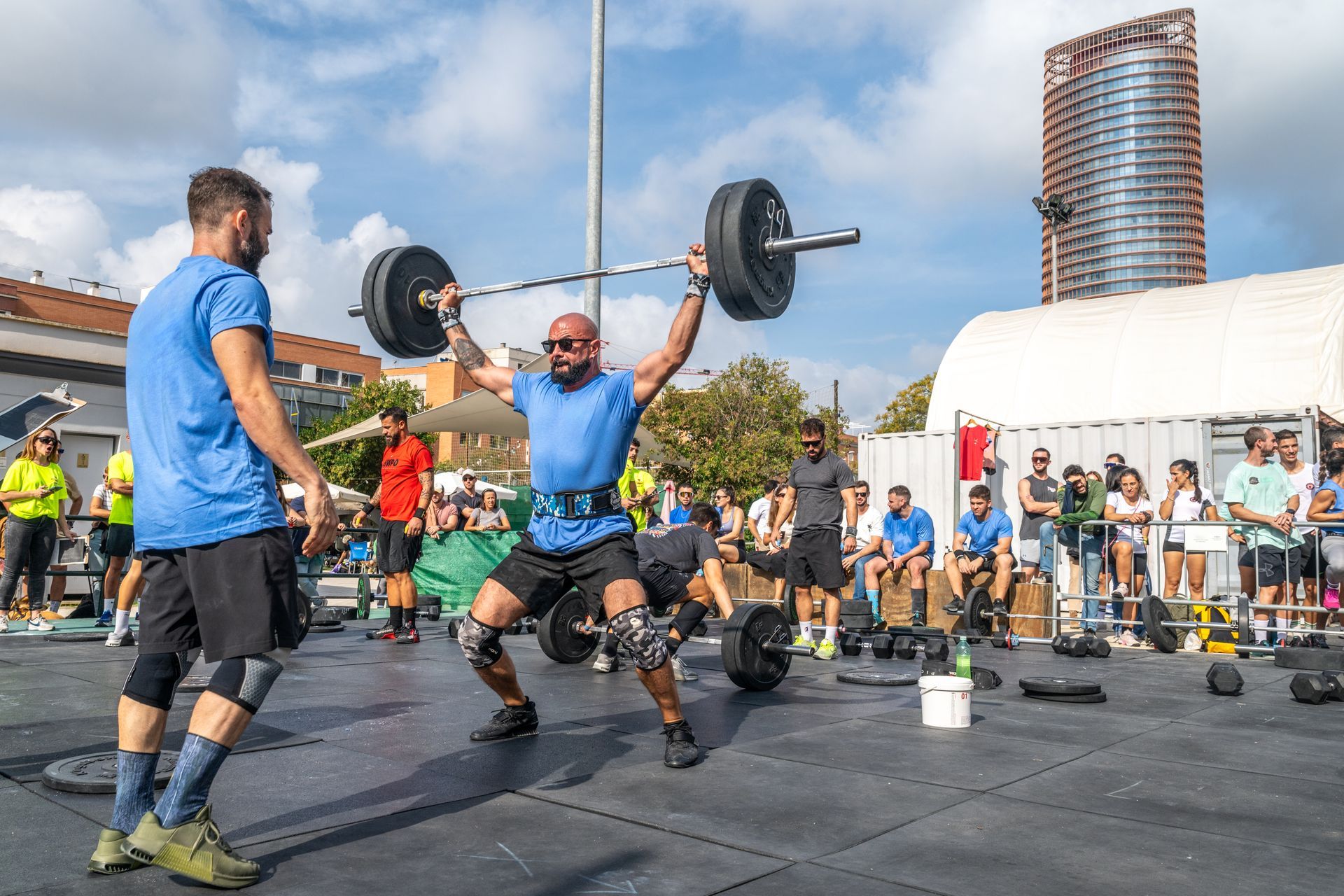 A man is lifting a barbell over his head while another man watches.