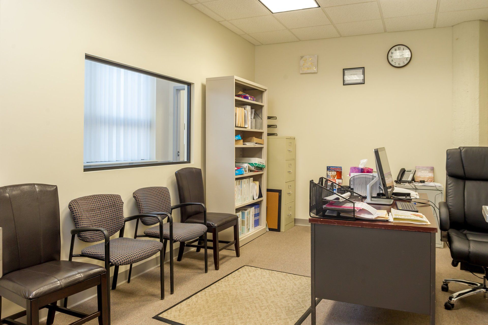 A waiting room with chairs , a desk and a computer.