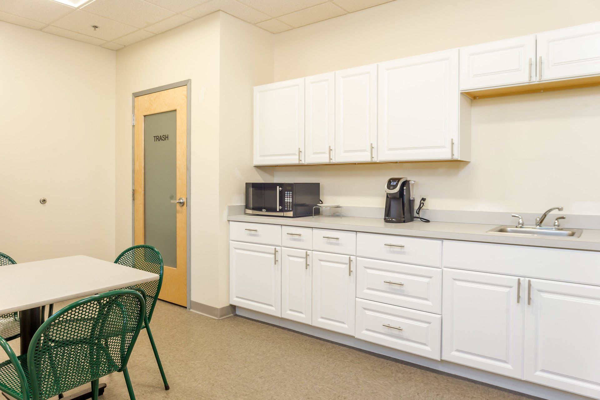 A kitchen with white cabinets and green chairs and a table