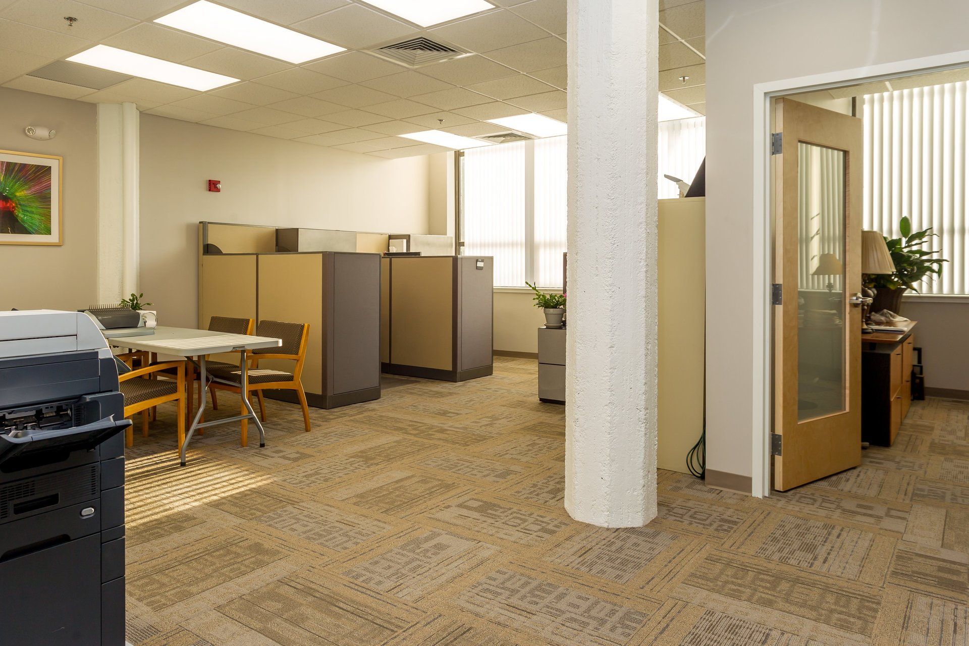 An empty office with cubicles , tables , chairs and a printer.