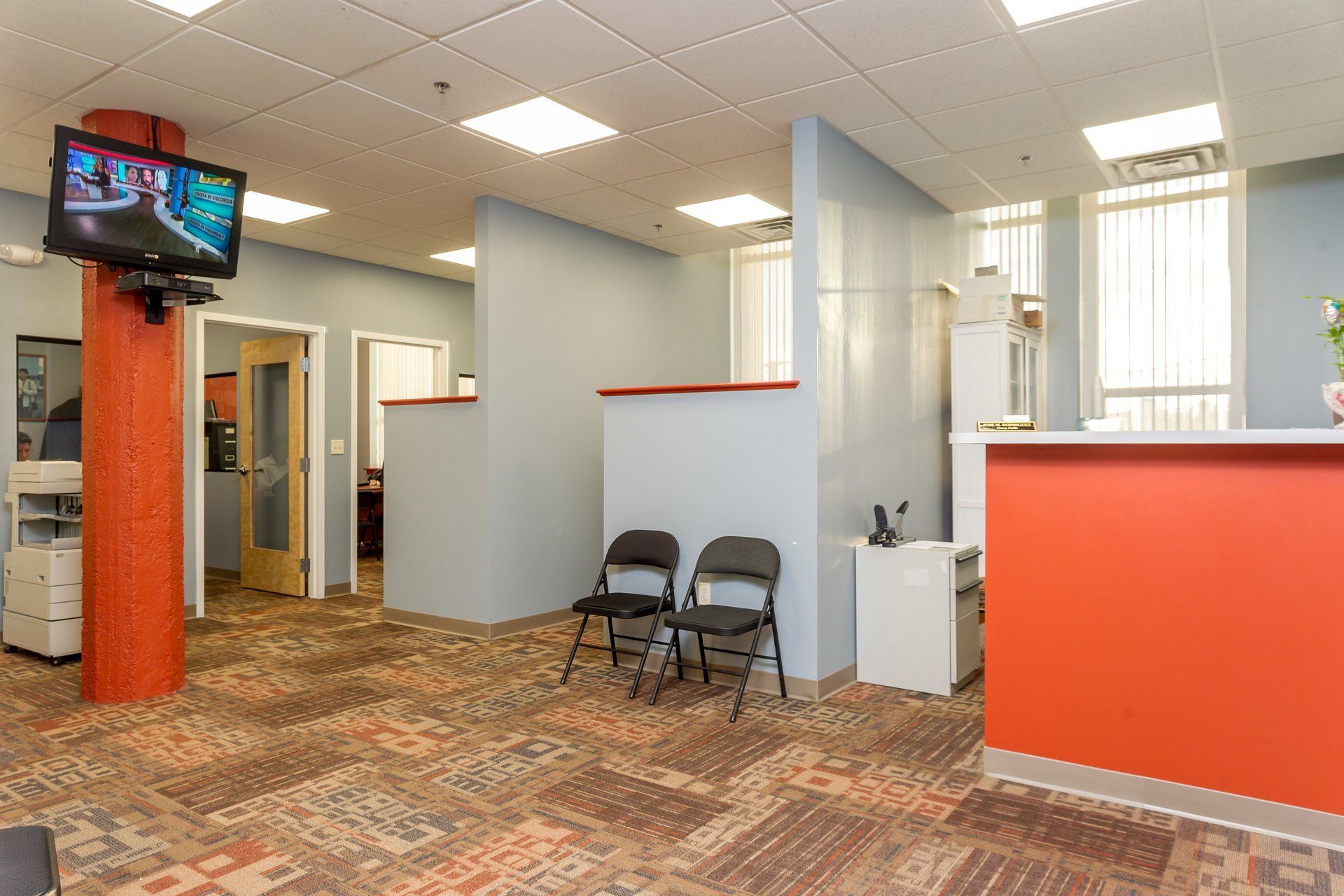 A waiting room with chairs and a tv on the wall.
